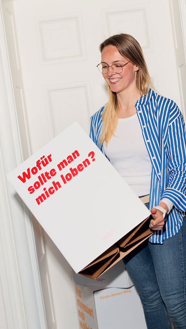 Eine Frau hält einen großen Würfel in den Händen und lächelt dabei.